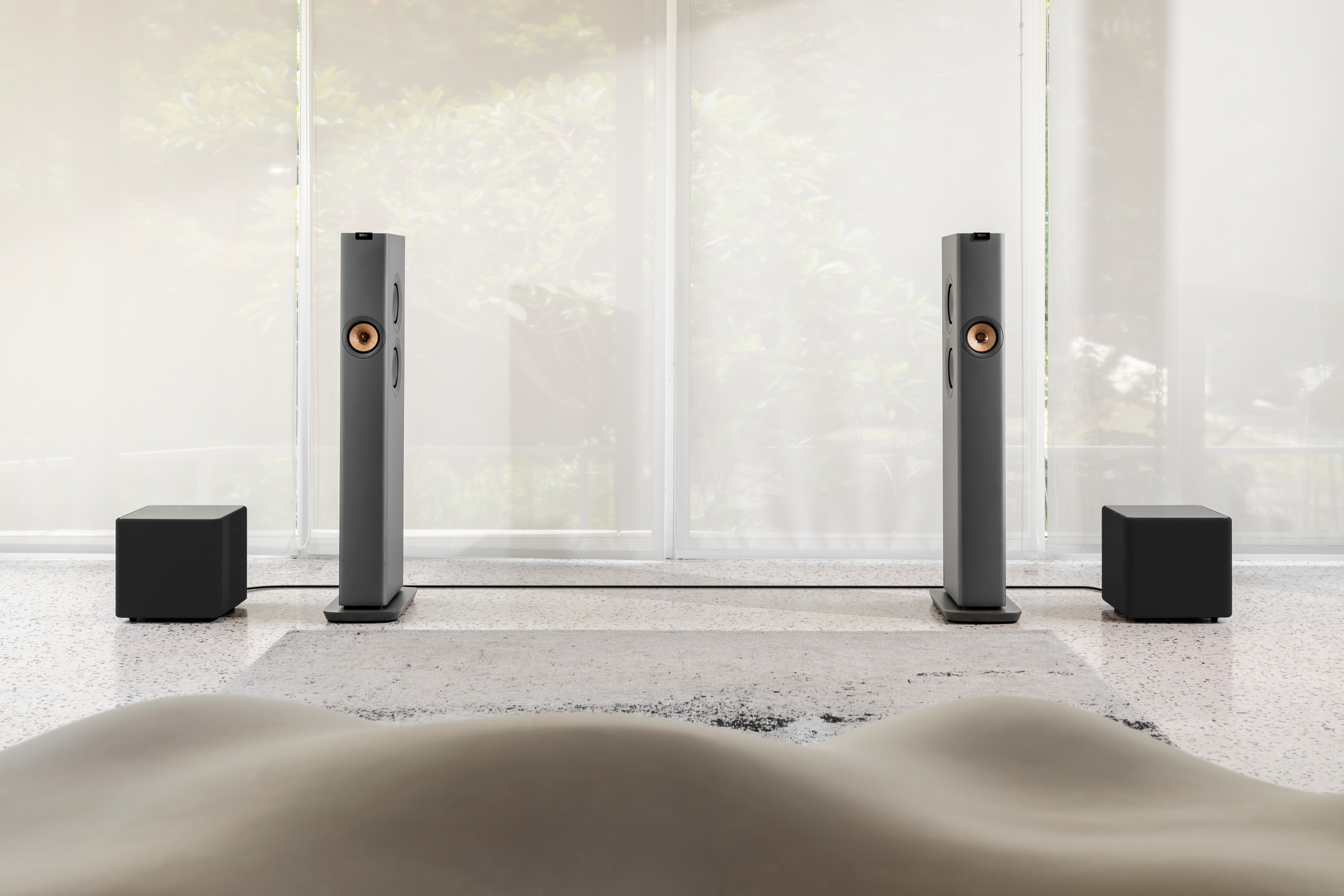 Une paire d'enceintes hi-fi sans fil sur pied Grey LS60 dans un salon, à côté de deux caissons de basses Kube 10 MIE