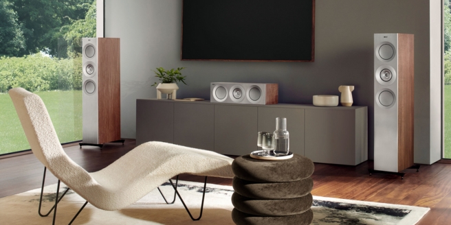 Moderne vloerluidsprekers met houtafwerking in een stijlvolle woonkamer met een designligstoel, neutrale tinten en grote ramen met uitzicht op de tuin.