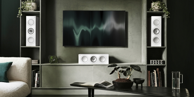 Installation home cinéma avec enceintes murales KEF blanches et voie centrale sous un téléviseur fixé au mur.