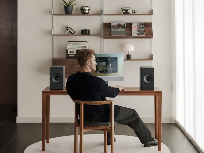 一名男子坐在办公桌正面，桌上摆放着电脑和 Coda W 扬声器。