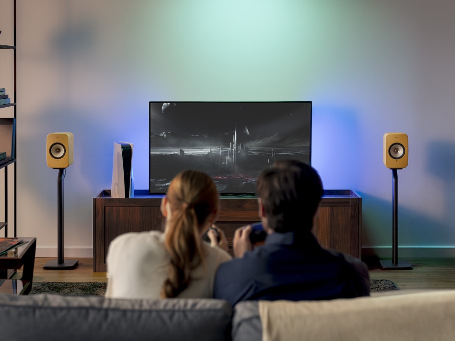 People playing with PlayStation console connected to TV and LSX II amber haze.