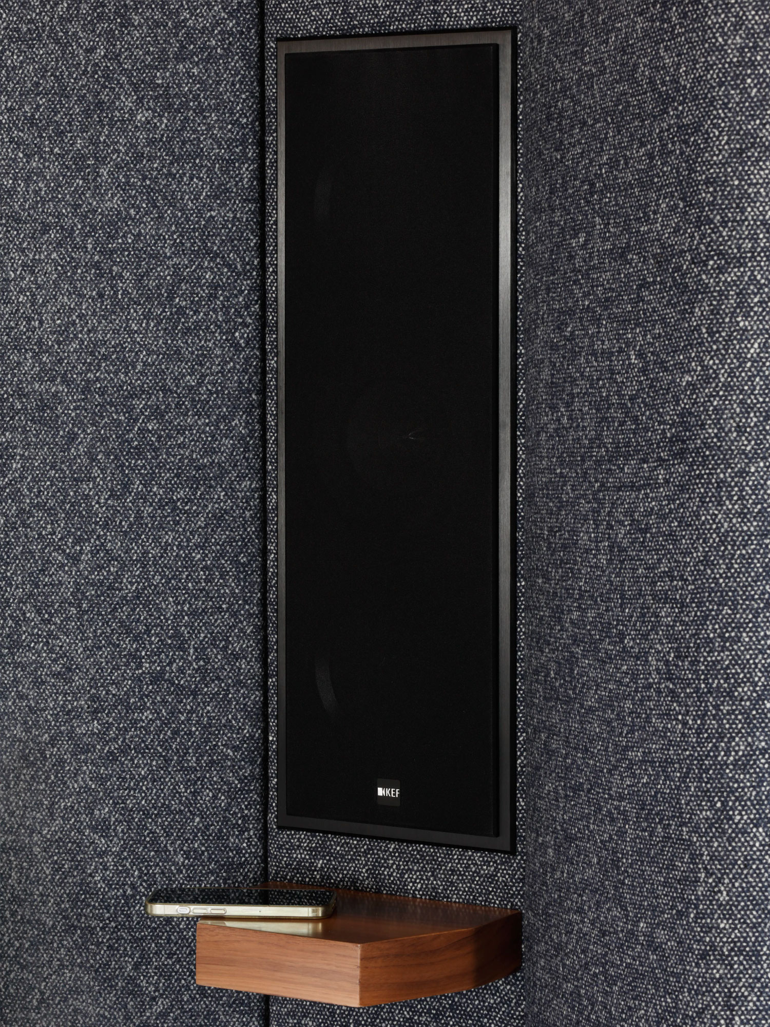 Detail of KEF's speakers with a black meth cloth grille and a mobile phone charging next to them