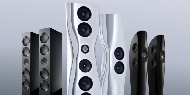 Une rangée d’enceintes HiFi KEF filaires, hautes et modernes, en finitions noire, argentée et blanche, disposées devant un fond minimaliste bleu clair.