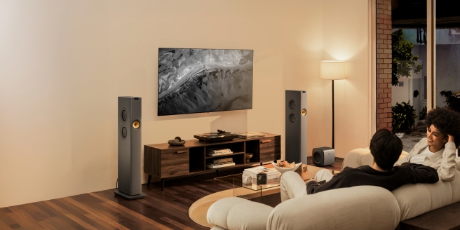 Gezin geniet van een thuisbioscoopervaring met KEF-luidsprekers en een wandgemonteerde tv in een gezellig verlichte woonkamer.