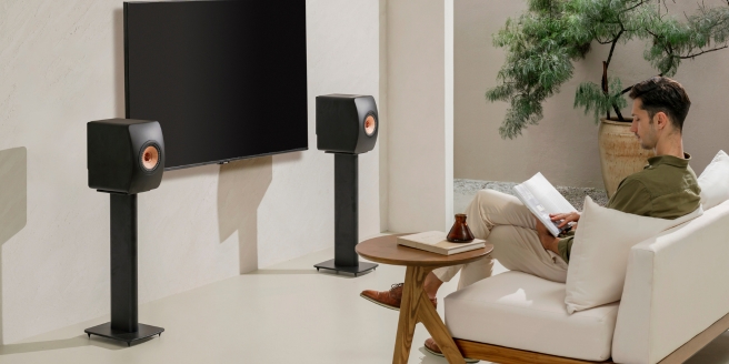 Man ontspant zich in een moderne woonkamer met KEF-vloerstaande luidsprekers en tv, als demonstratie van een high-res audiosysteem.