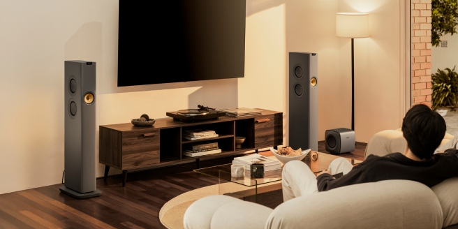 Persoon geniet van een homecinema-opstelling met KEF-vloerstaande luidsprekers en een grote tv.