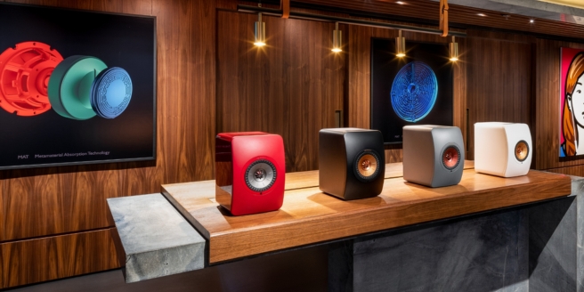 Presentatie van KEF-draadloze luidsprekers in verschillende kleuren op een houten toonbank in een showroom.