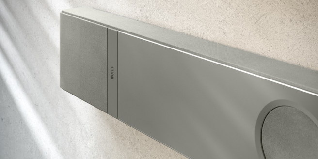 Nahaufnahme einer eleganten silbernen KEF Soundbar an einer strukturierten Wand, die das minimalistische Design und die hochwertige Verarbeitung hervorhebt.