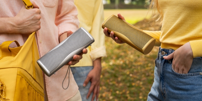 Drei Personen halten tragbare kabellose Lautsprecher in einem Park.