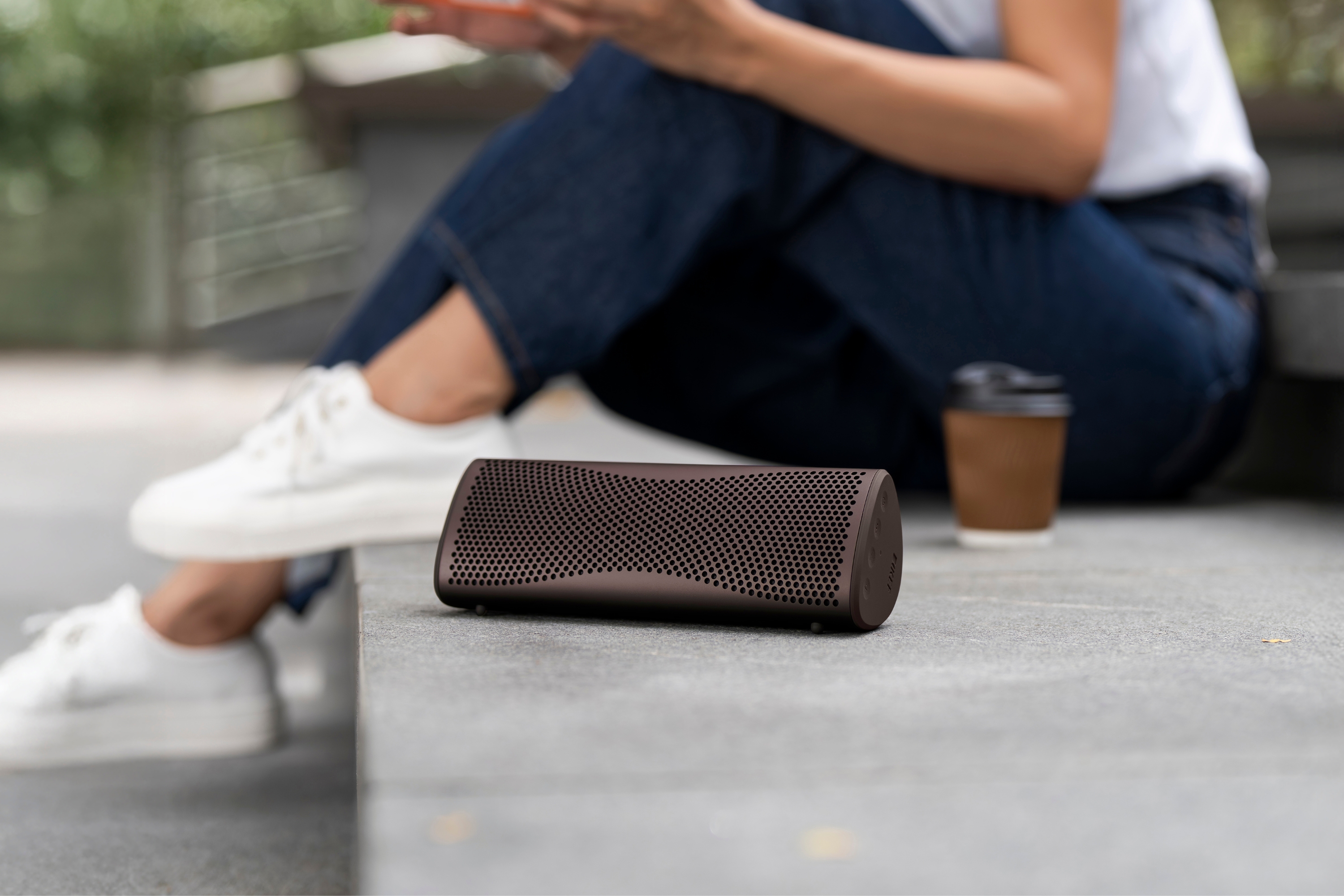 Tragbarer kabelloser Lautsprecher steht auf Betonstufen neben einem Coffee-to-go-Becher.