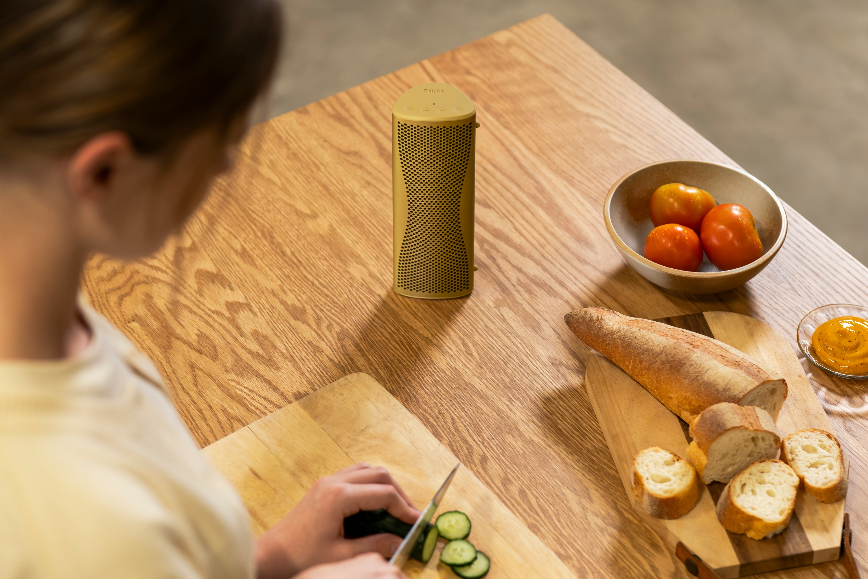 Tragbarer Lautsprecher steht auf einem Holzküchentisch neben geschnittenem Brot und Gemüse bei der Essenszubereitung.
