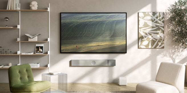 Hedendaagse woonkamer met een tv die een landschap toont, groene accentstoel, open planken en zachte neutrale tinten.