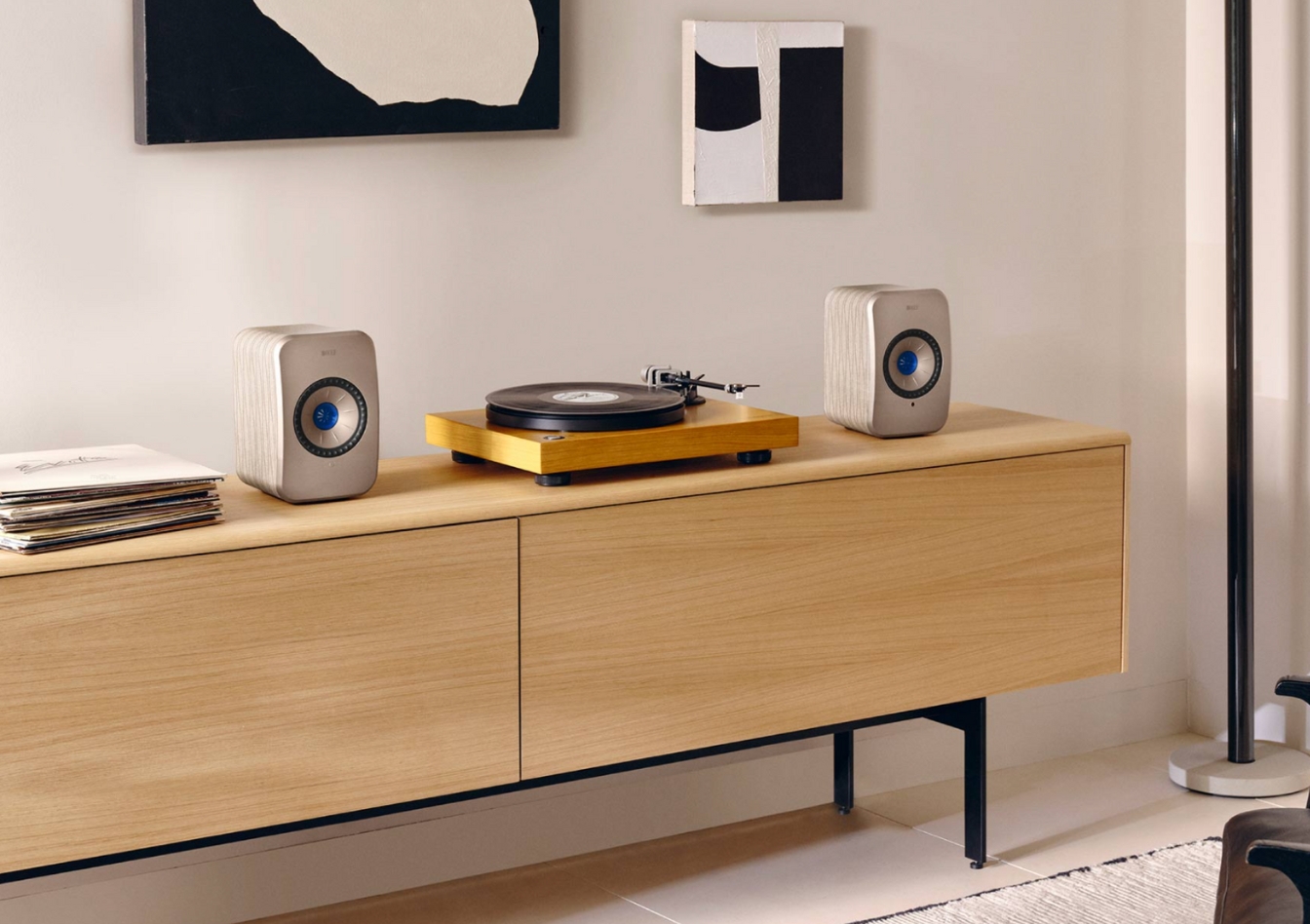 Compact bookshelf speakers with a record player on a light wooden sideboard in a modern living room with abstract wall art.