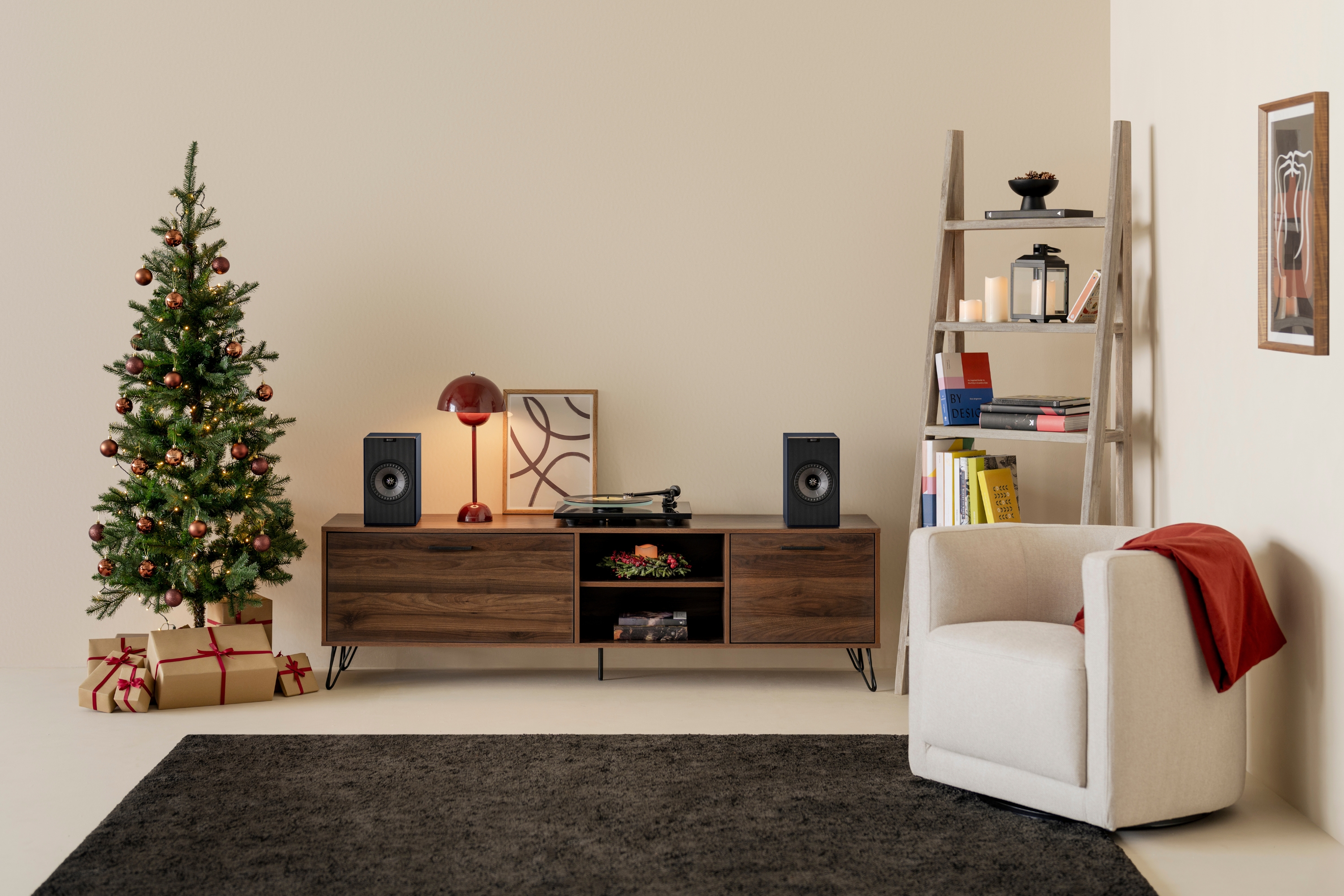 Minimalistische woonkamer met kerstversiering, zwarte boekenplankluidsprekers, een platenspeler en een kleine boom met koperen kerstballen en cadeaus.