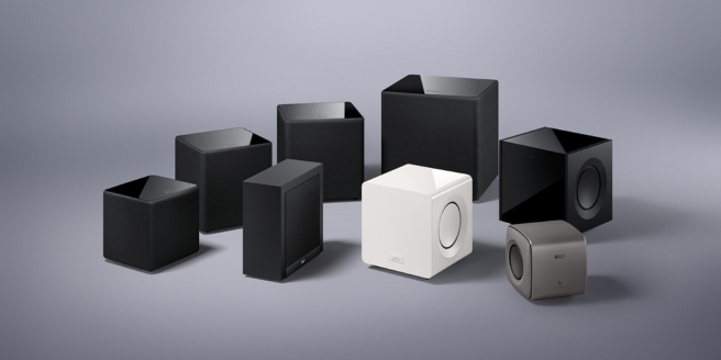 Collectie KEF subwoofers in diverse maten en afwerkingen op een neutrale grijze achtergrond