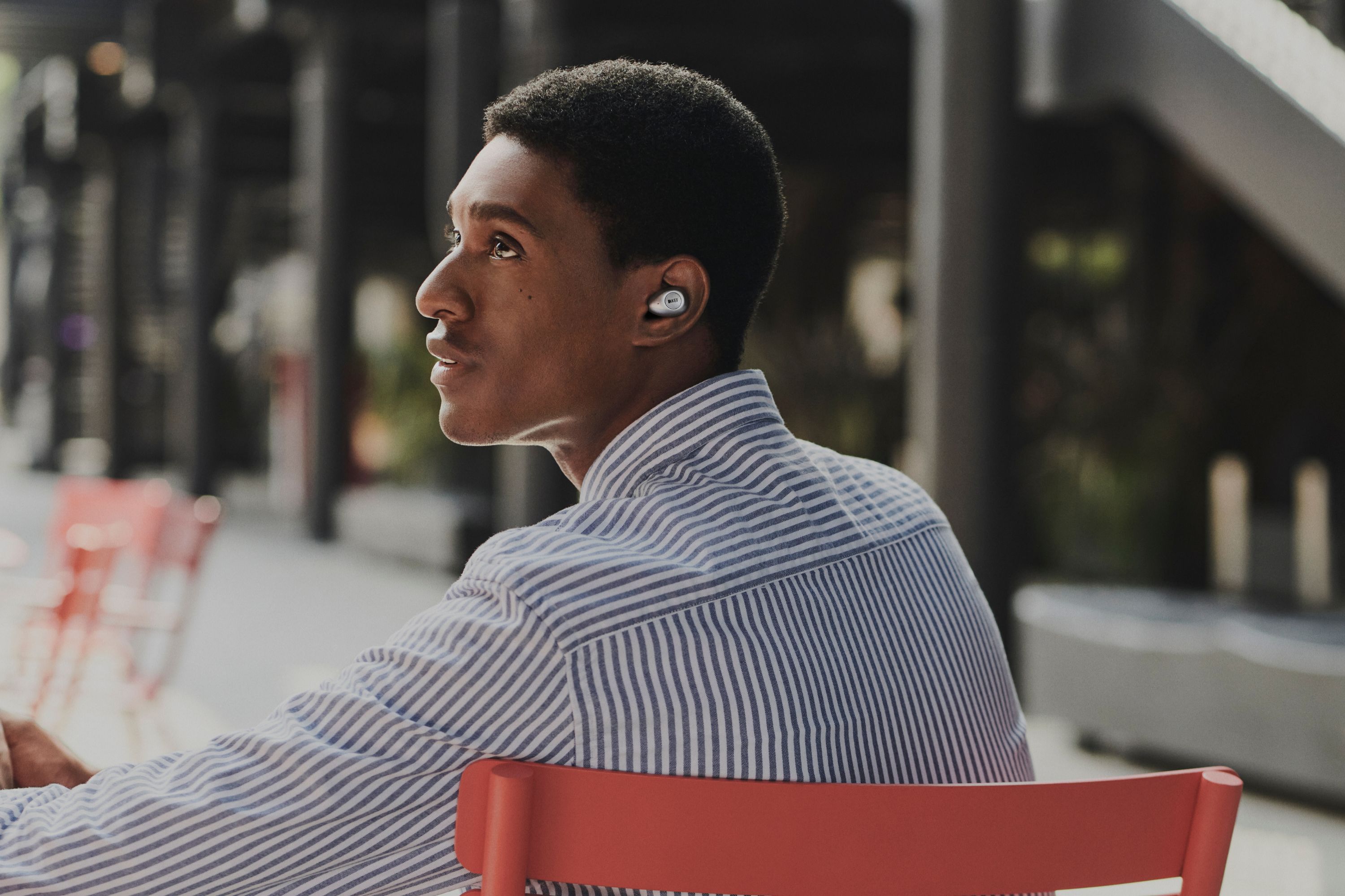 A man outside in the city wearing a silver KEF Mu3 earphones 