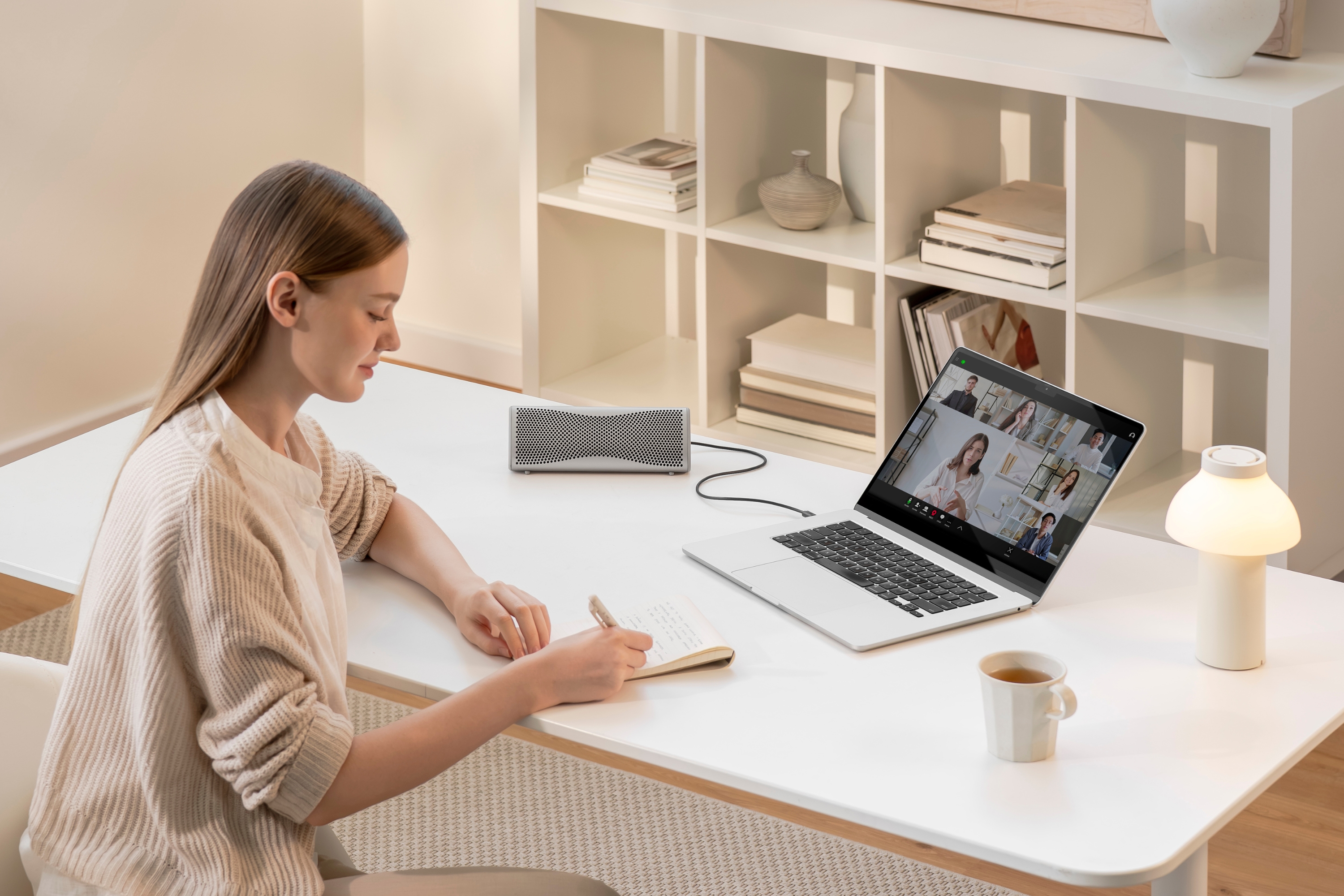A Bluetooth speaker connected to a laptop during an online meeting in a home office setting.