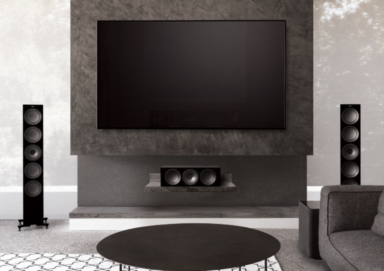 Modern living room with a wall-mounted flat-screen TV, flanked by two floor-standing KEF speakers, showcasing optimal TV height placement above a sleek media console.