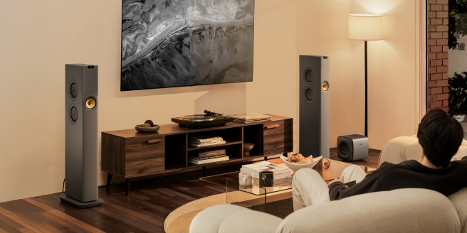 Cosy home cinema setup featuring KEF speakers, ambient lighting, and a couple relaxing on a sofa watching TV in a warmly lit living room.