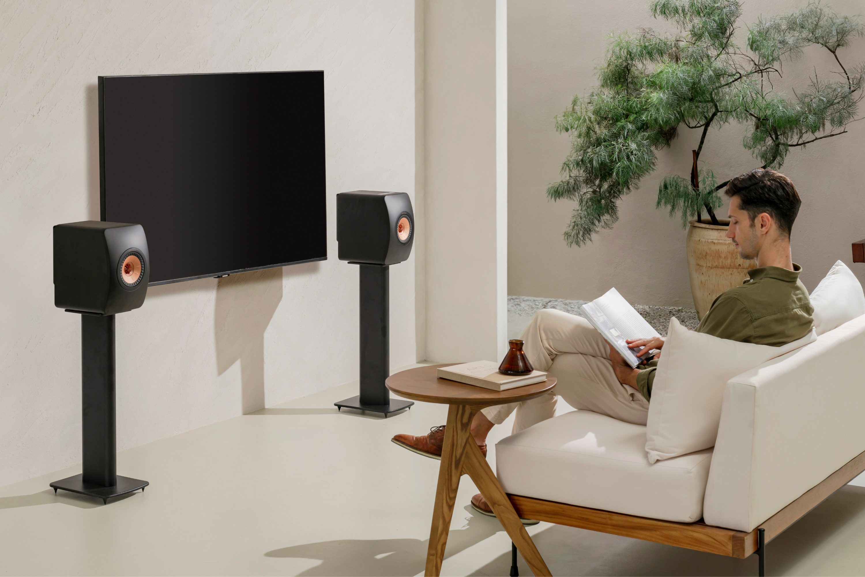 A man reading his book in front of a pair of LS50 WII Black speakers placed on a floor stand
