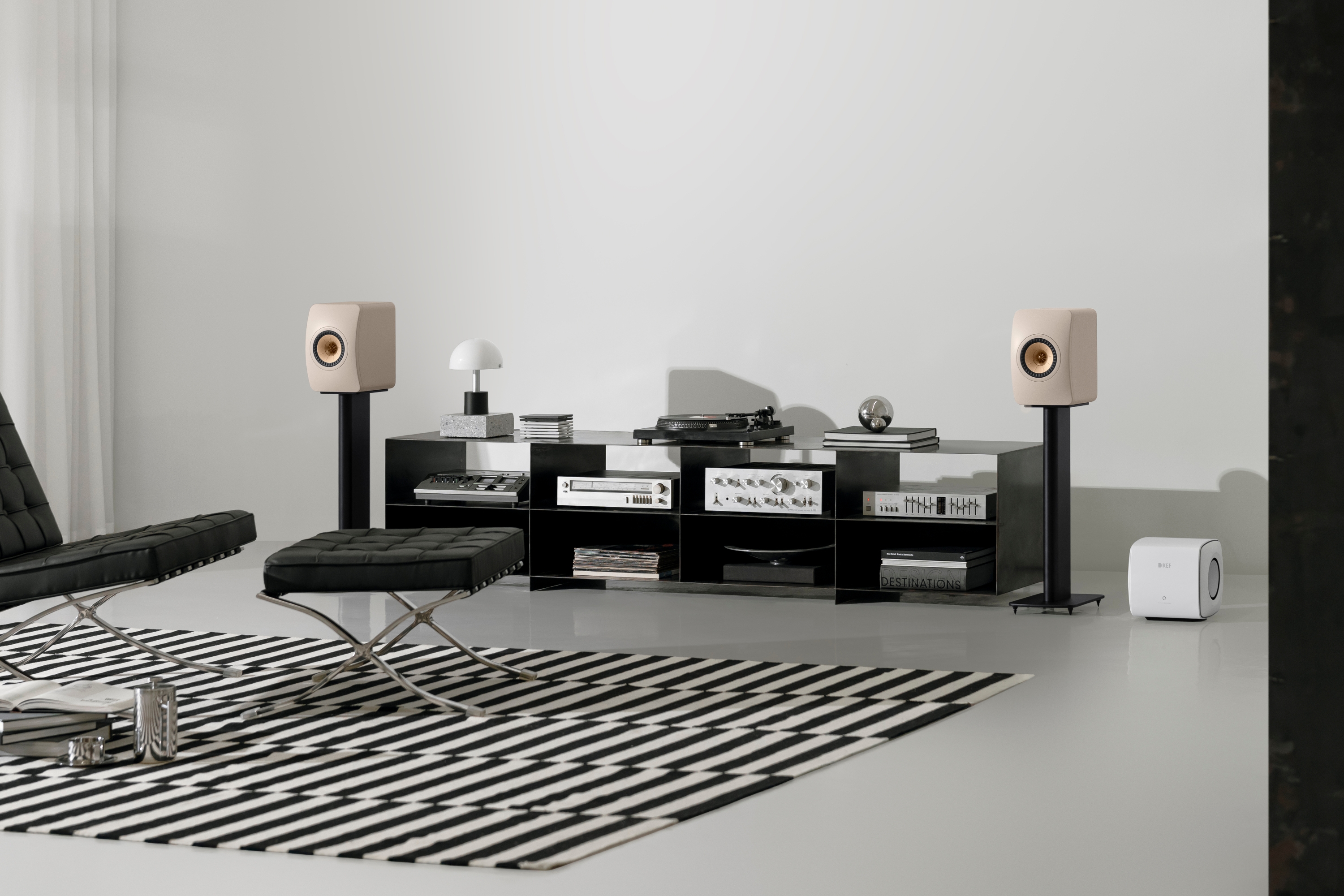 Pair of LS50 Wireless II Mineral White speakers placed between a sideboard next to a KC62 Subwoofer