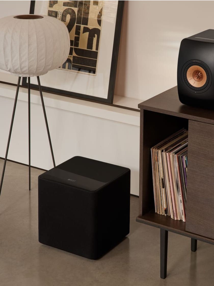 Caisson de basses noir posé au sol, à côté d’une enceinte LS50 Wireless posée sur un buffet.