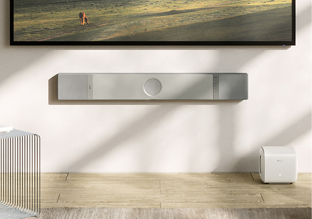 Modern living room showcasing a floating island scene on a wall-mounted TV, with a sleek grey XIO Soundbar and white KC62 subwoofer setup beneath.