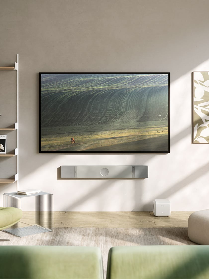 Sunny living room with TV and wall mounted silver XIO soundbar and white KC62 subwoofer.