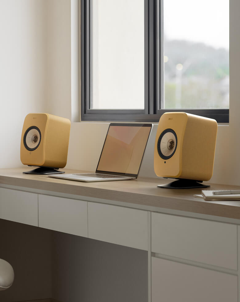LSX II-luidsprekers in Amber Haze op een bureau naast een laptop.