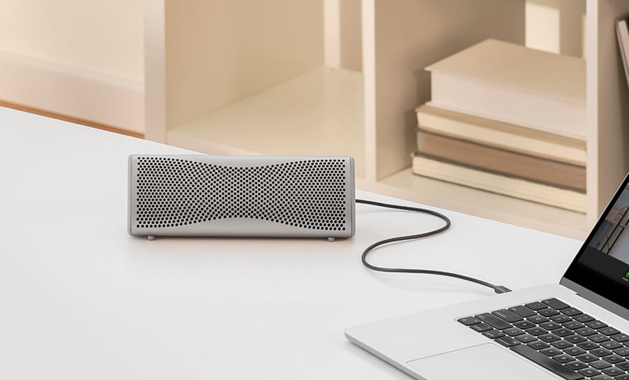 Enceinte Bluetooth Muo argentée utilisée avec un ordinateur portable via connexion USB-C.